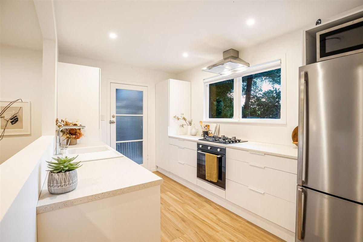 White kitchen cabinets with a cream benchtop, cooktop and rangehood